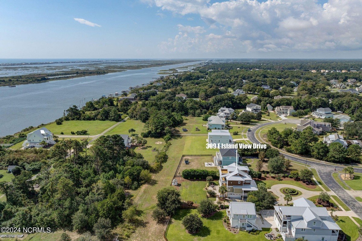 Aerial view shows house near water with other houses nearby.