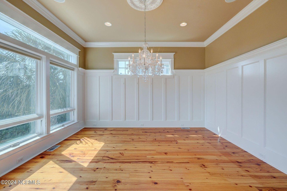 Room has hardwood floors, white wainscoting, and chandelier.