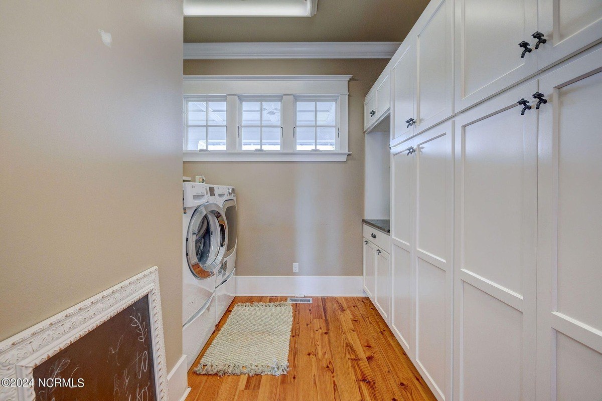 Laundry room has hardwood floors, white cabinets, and washer and dryer.