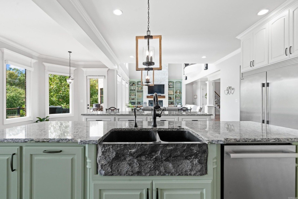 Kitchen island with a farmhouse sink and granite countertops, overlooking a living area with a fireplace.