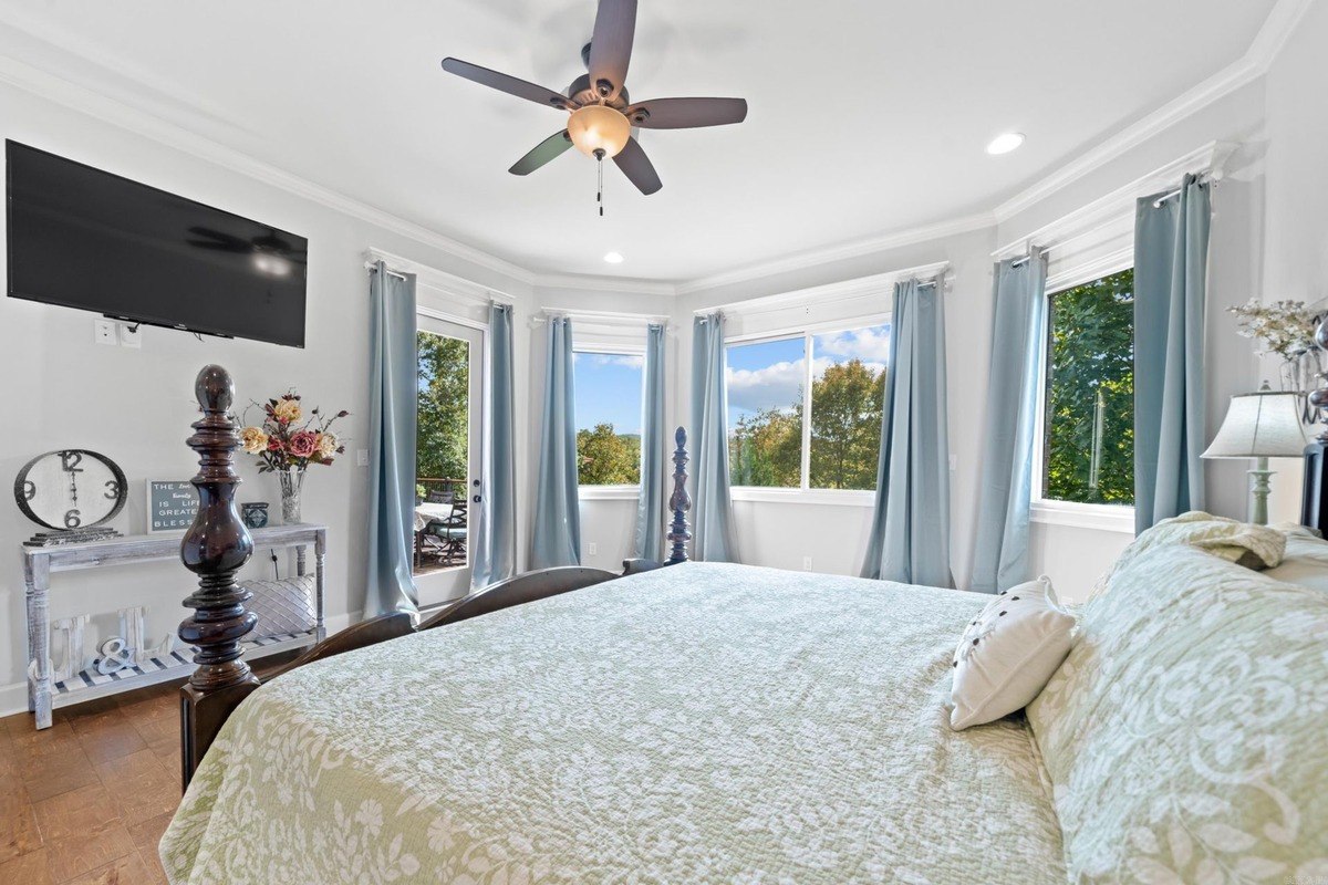 Master bedroom with king-size bed, ceiling fan, and multiple windows offering a view of nature.