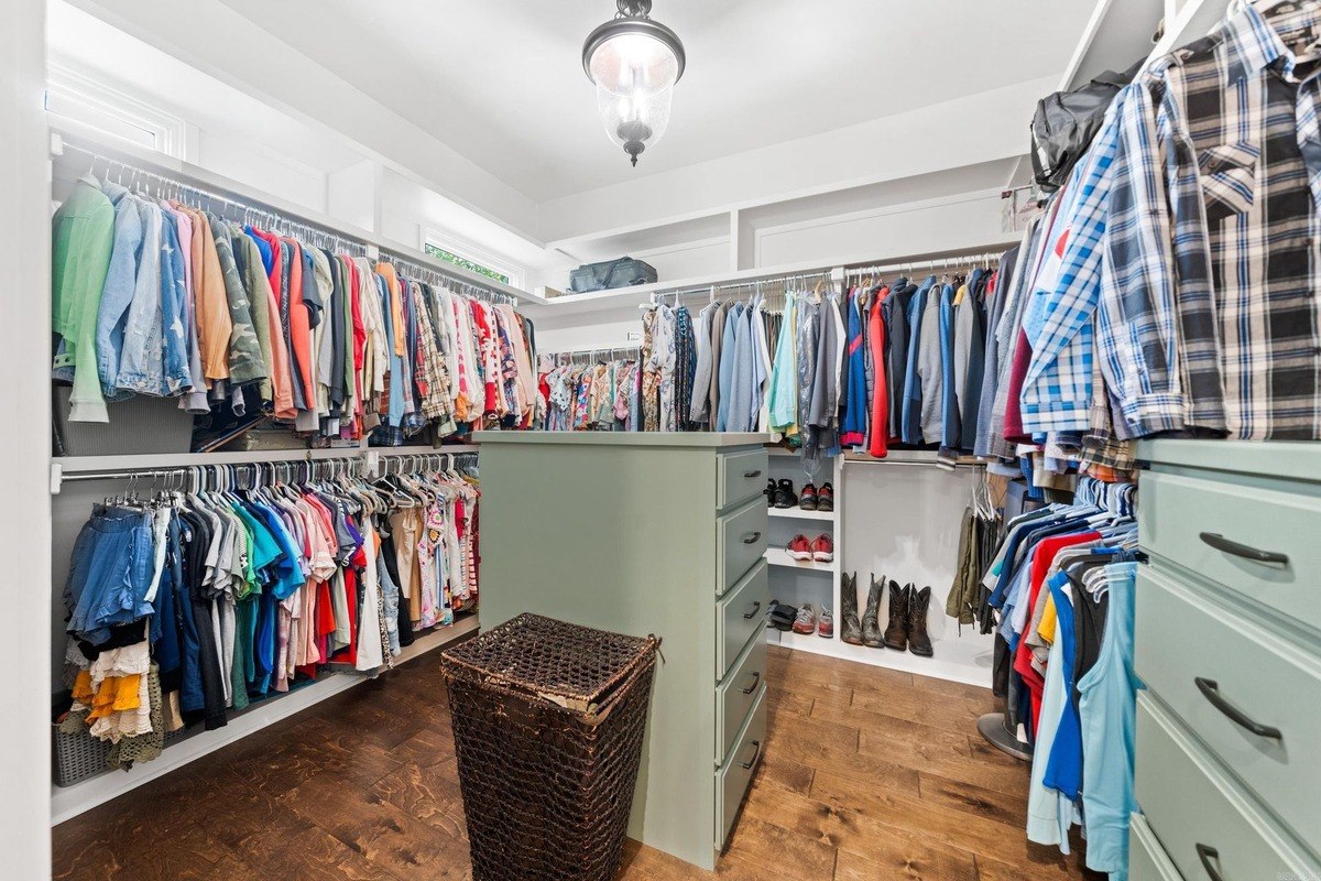 Walk-in closet with clothing organized on shelves and hanging rods, plus a central dresser.