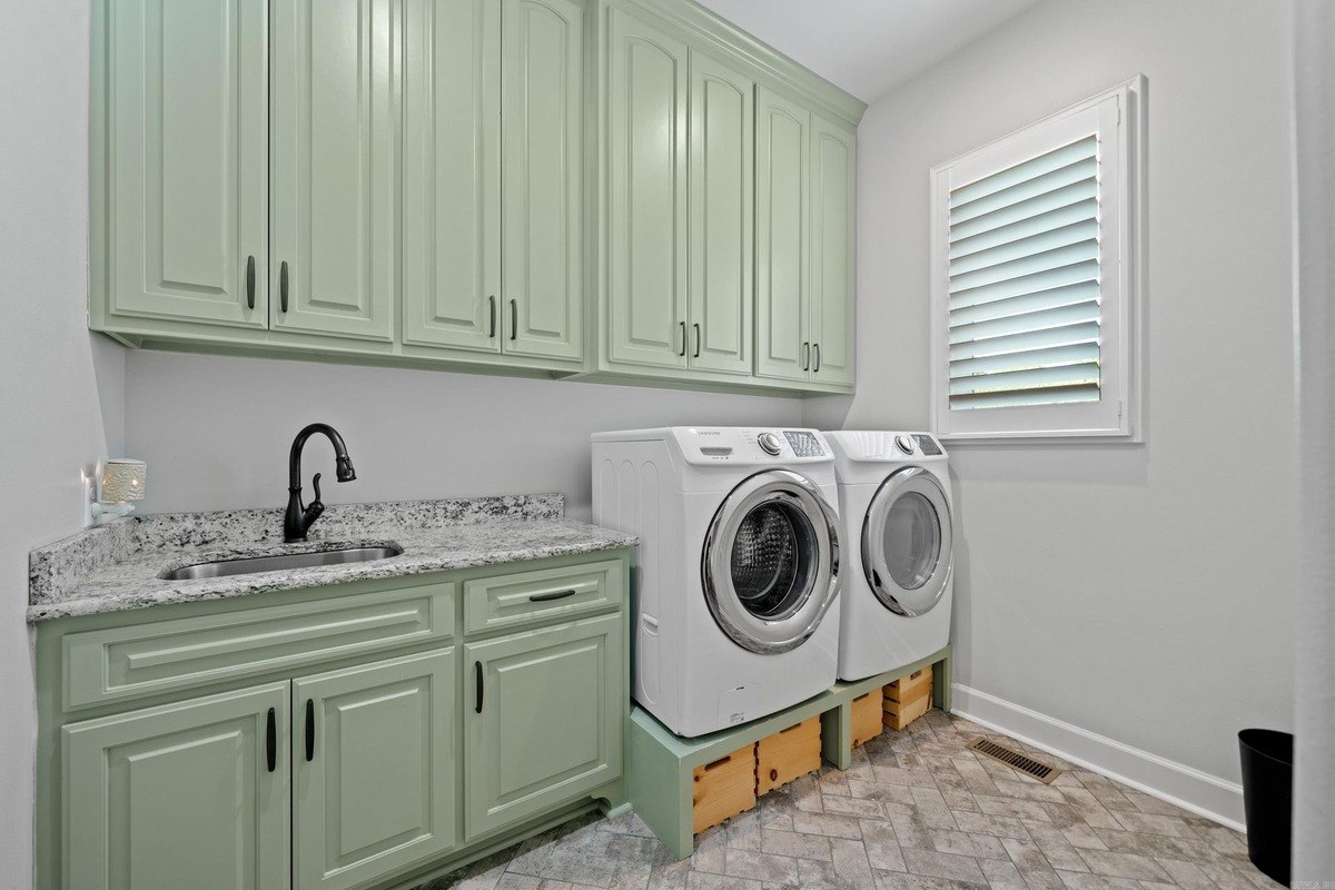 Laundry room with light green cabinets, granite countertops, and a utility sink.