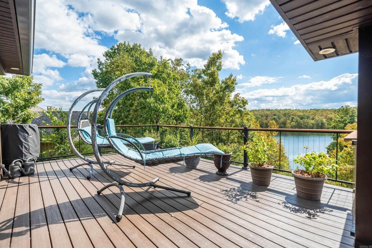 Deck with hanging chairs and potted plants overlooking a lake and trees.