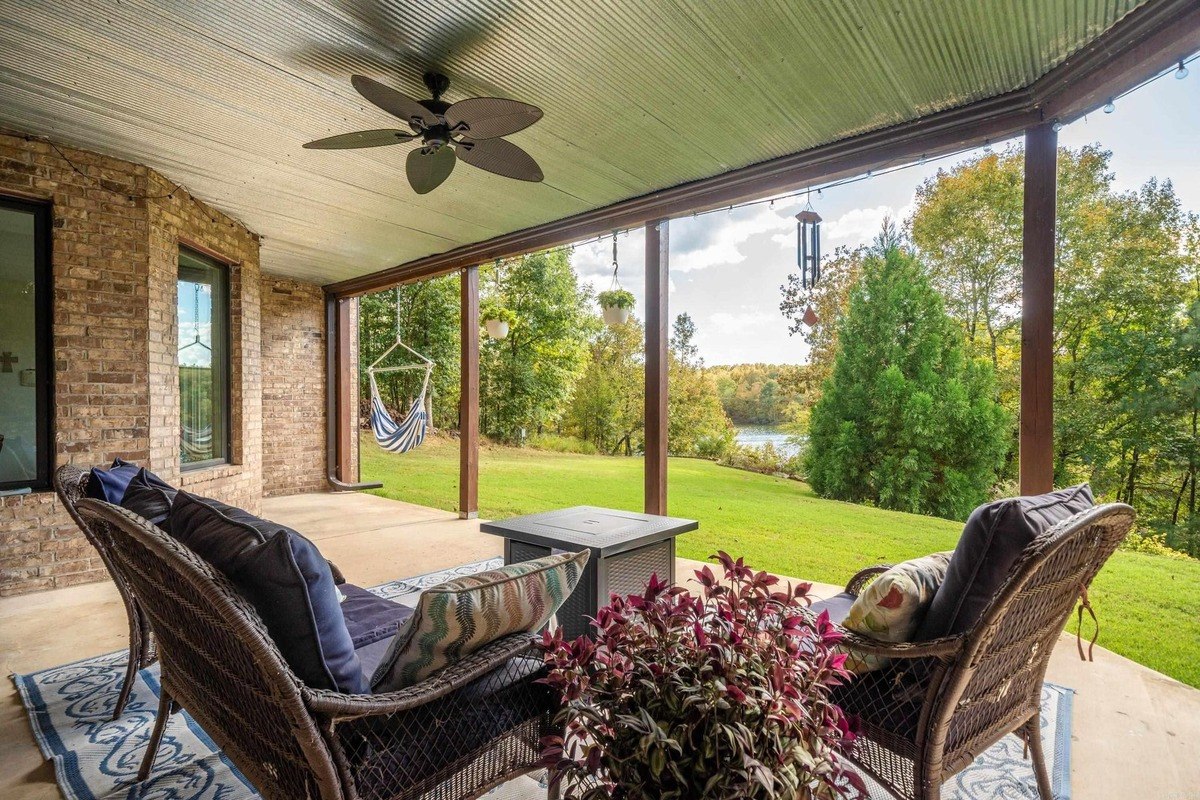 Covered patio with wicker furniture and a view of a lake and trees.