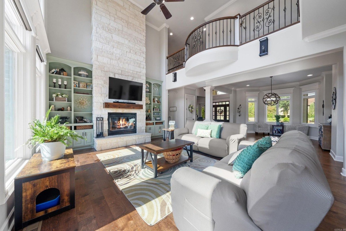 Large living room with a stone fireplace, hardwood floors, and a second-story balcony.