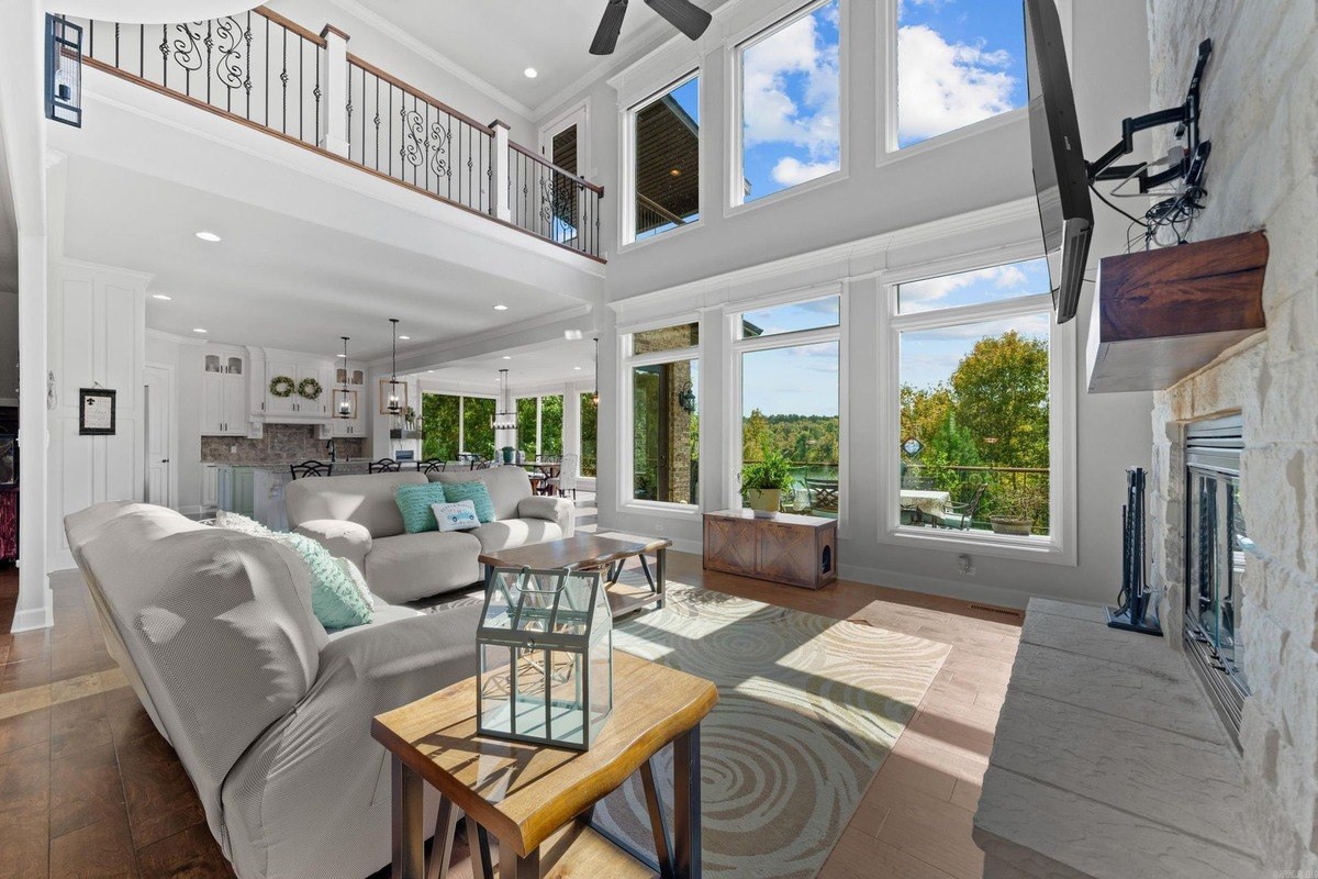 Living room with high ceilings, large windows offering a scenic view, and a second-story balcony.