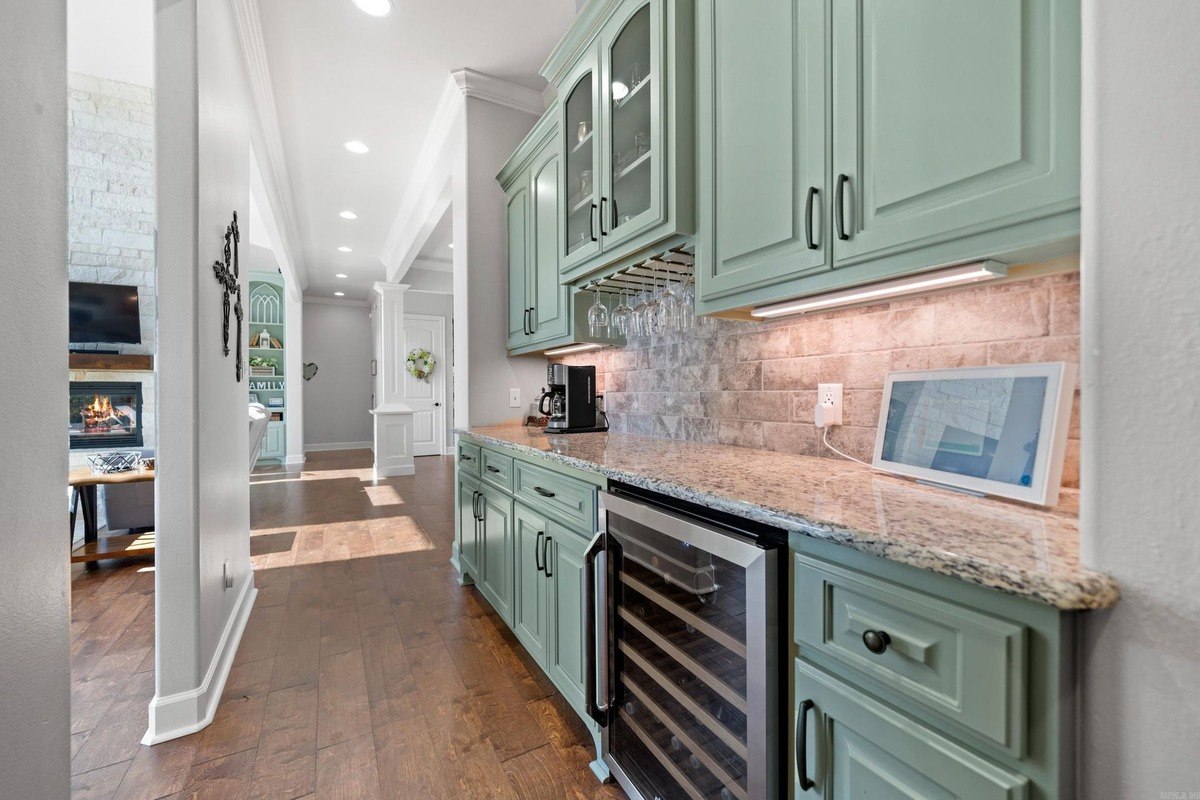 Kitchen wet bar with light green cabinets, granite countertops, and wine cooler.