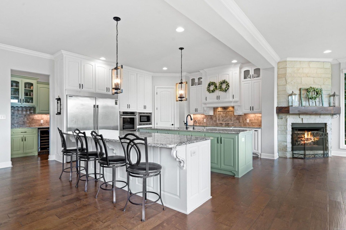 Large kitchen with white and light green cabinets, granite countertops, and a kitchen island with seating.