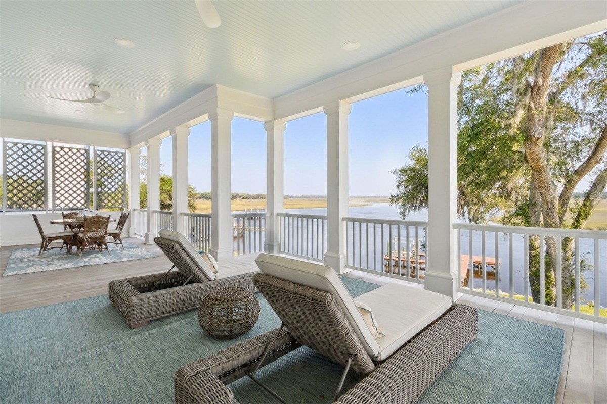 Porch has wicker lounge chairs and a dining set with a view of water.