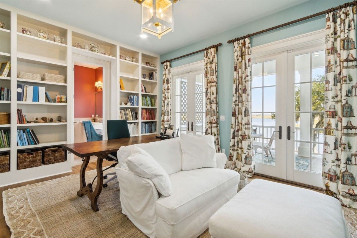 Library has built-in bookshelves, a white slipcovered sofa, and French doors leading to a porch.