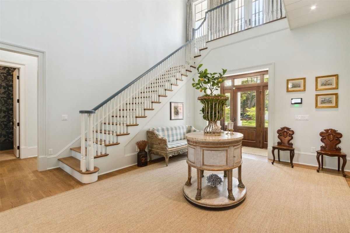 Grand foyer has a large staircase, ornate table, and seating area.