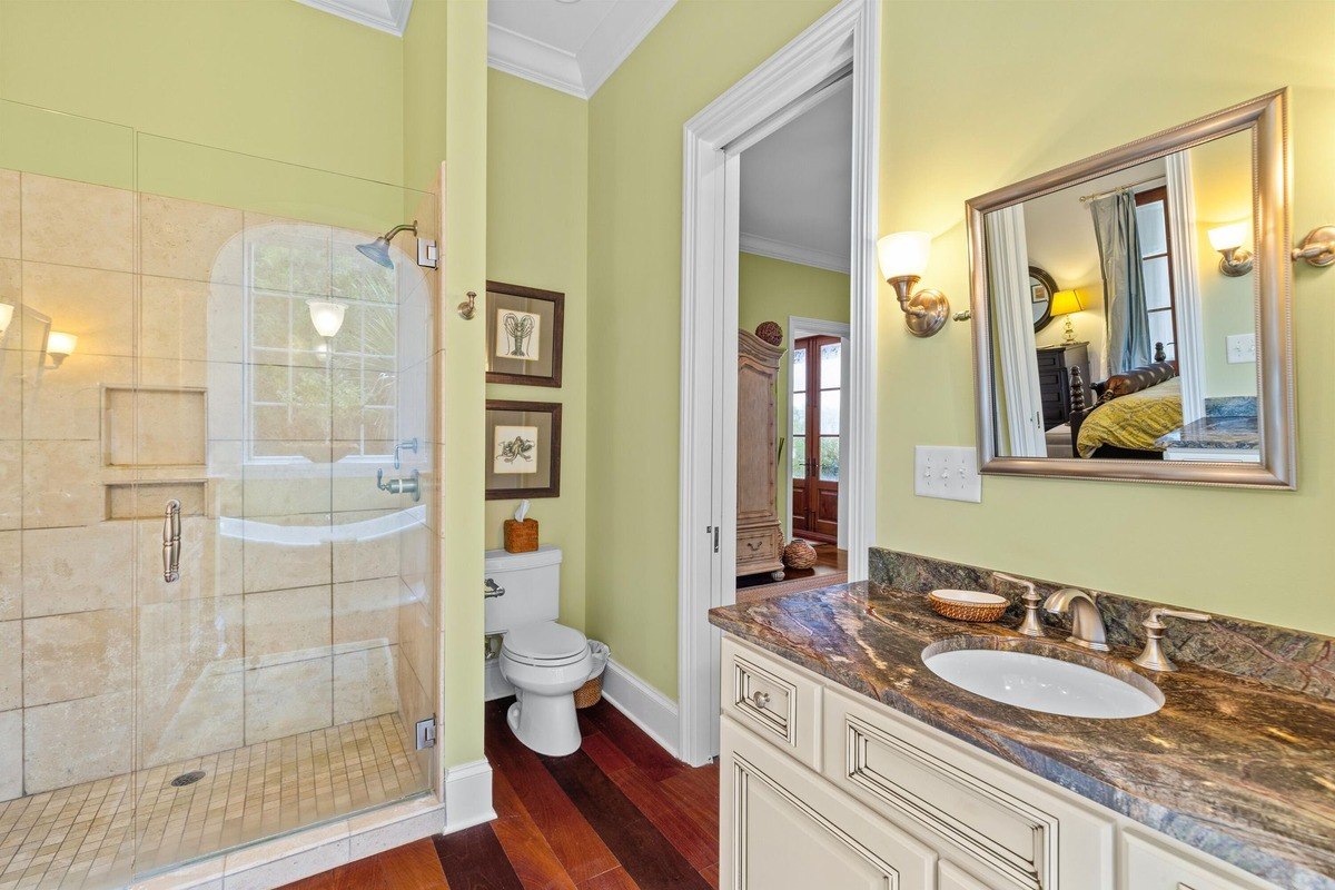 Bathroom features a glass shower, toilet, vanity with granite countertop, and light green walls.