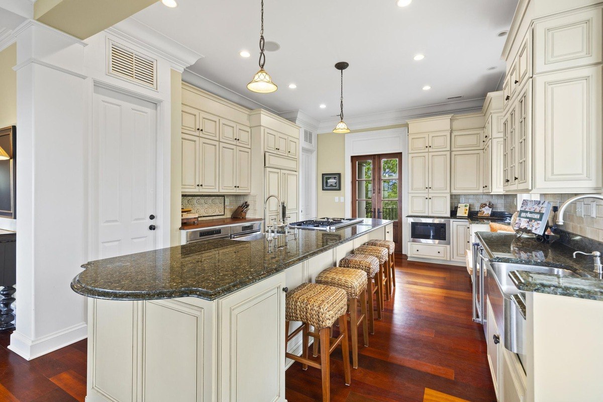 Kitchen features a large island with granite countertops, off-white cabinets, and hardwood floors.