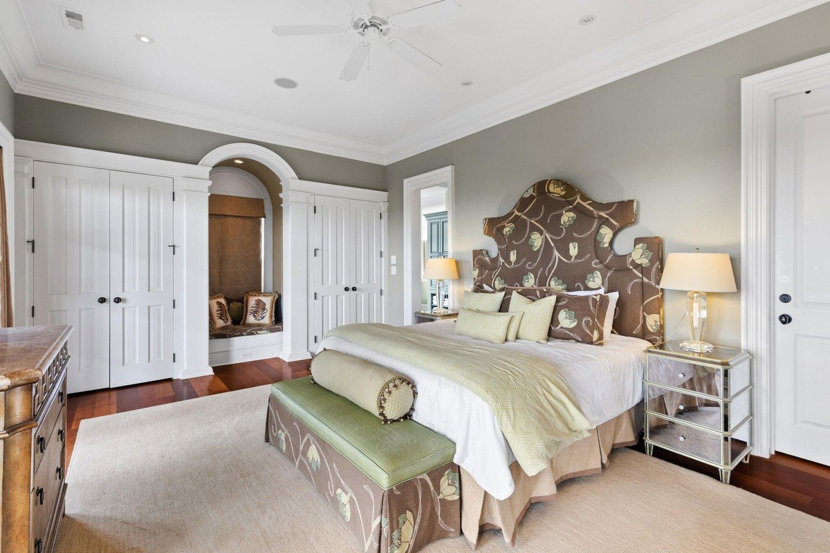 Master bedroom features a large bed with a patterned headboard, a seating bench at the foot of the bed, and hardwood floors.