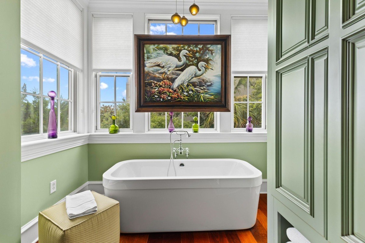 Bathroom features a freestanding tub, light green walls, and a painting of birds above it.