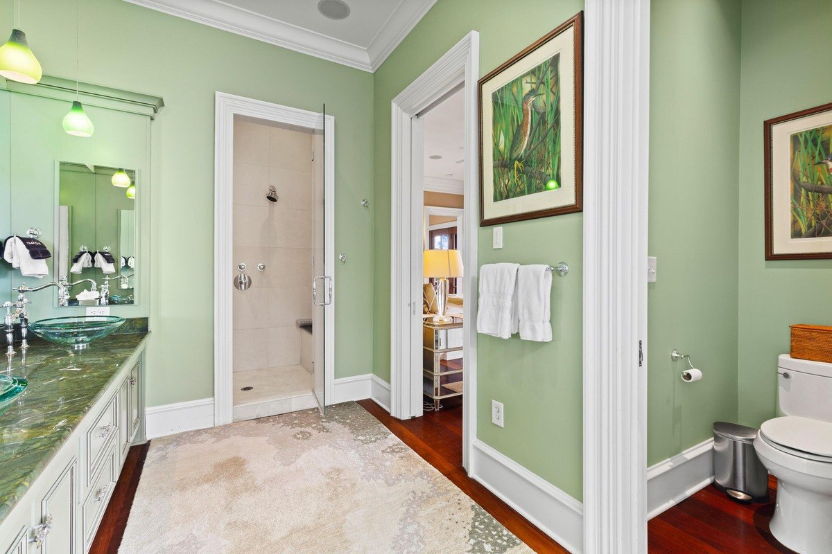 Bathroom has light green walls, a glass-enclosed shower, and a marble-topped vanity.