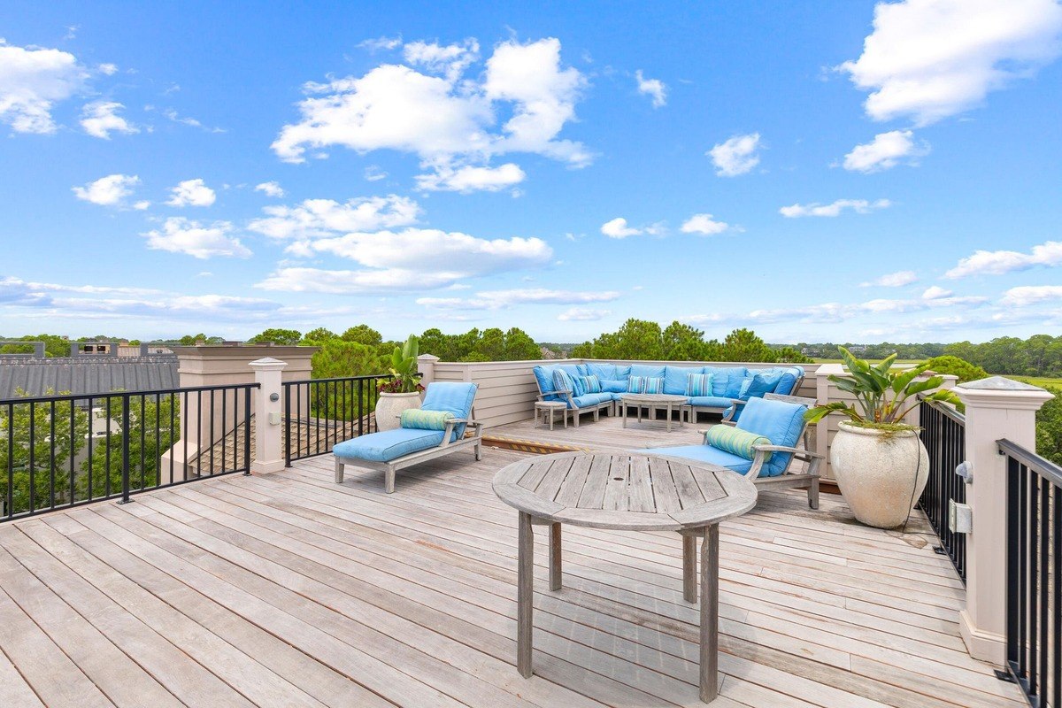 Rooftop deck features lounge chairs, a sectional sofa, and a wooden table, overlooking a scenic view.