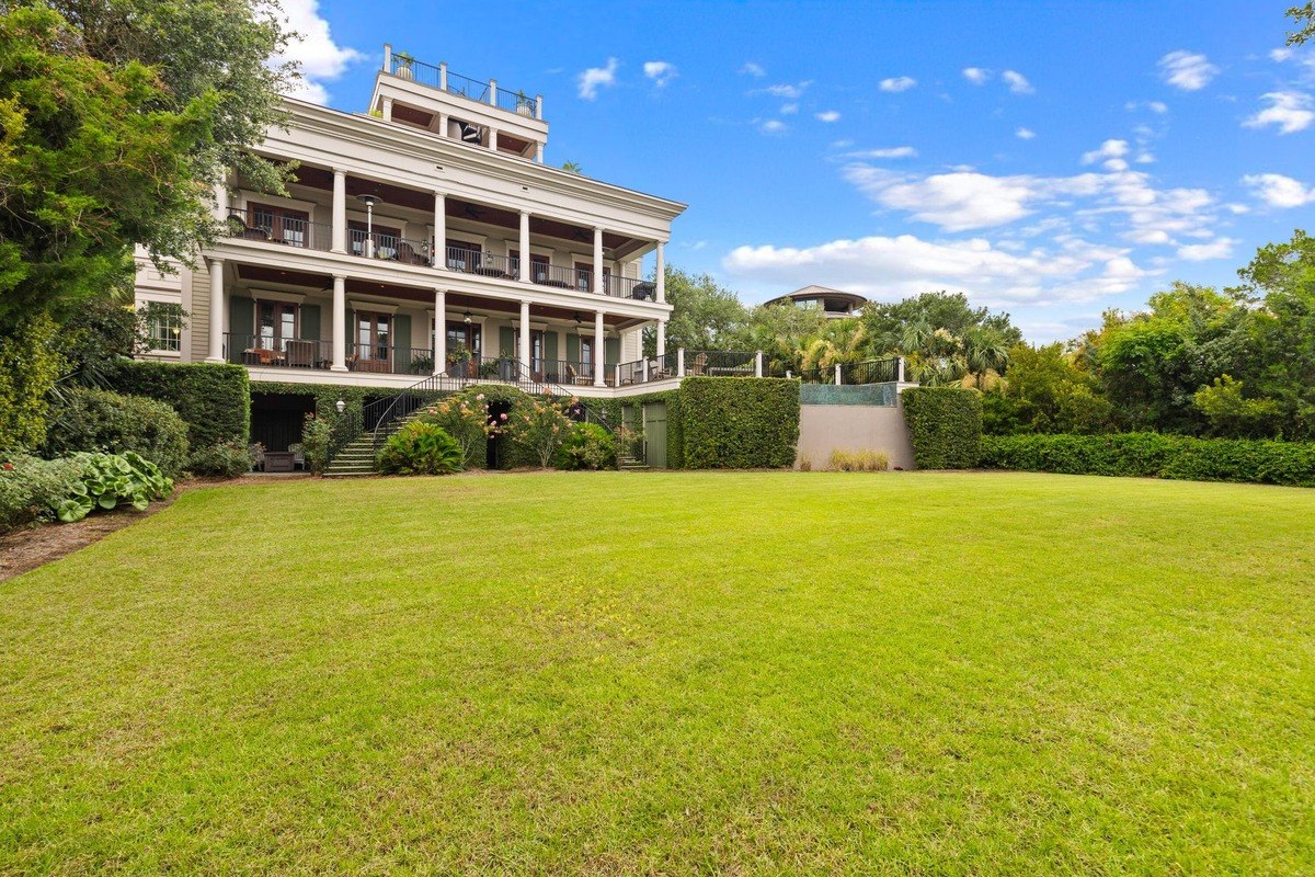 Large house with multiple levels and a wrap-around porch sits on a spacious lawn.