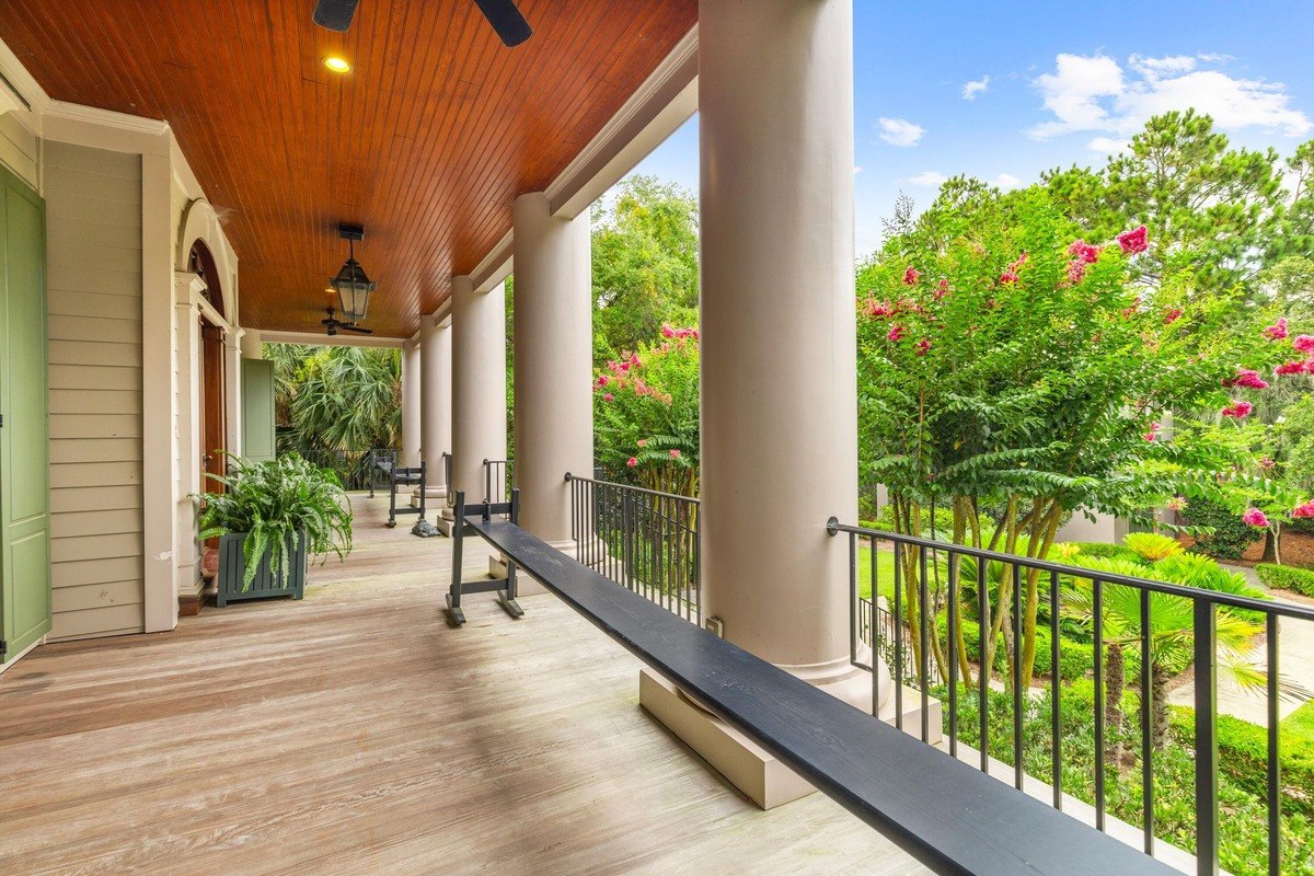 Long porch with wooden floors and columns overlooks a garden with flowering trees.