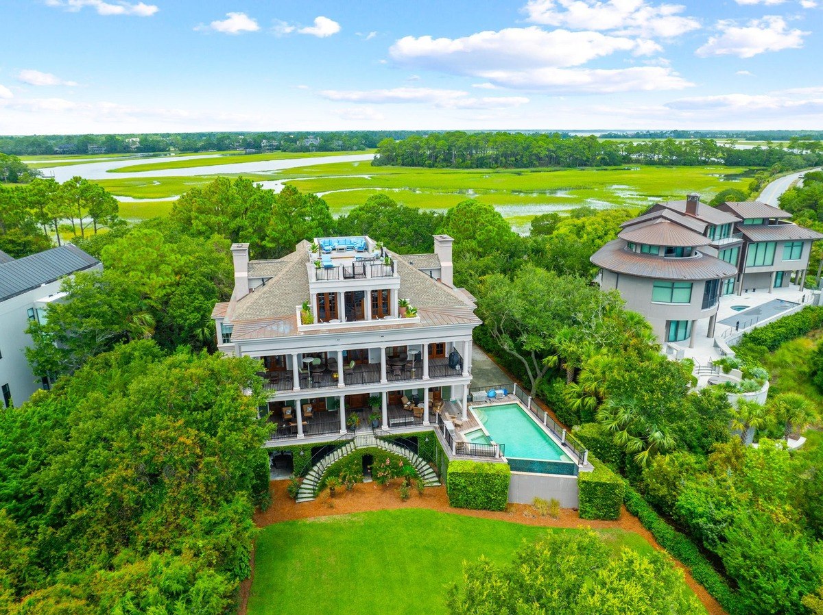 Large multi-story house with a pool and rooftop deck overlooks a marsh.