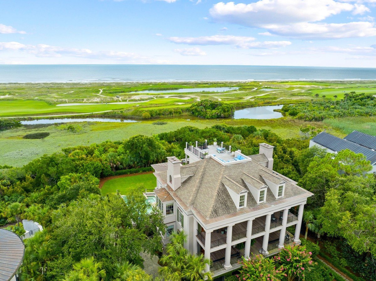 Large house with a rooftop pool and multiple balconies overlooks a golf course and ocean.