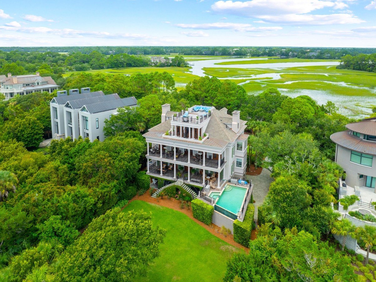 Large house with a pool and rooftop deck overlooks a marsh and waterway.