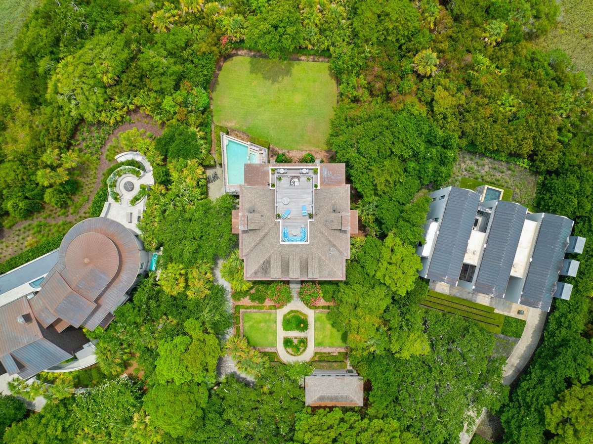 Aerial view shows several houses nestled within lush greenery, with pools and landscaped gardens.