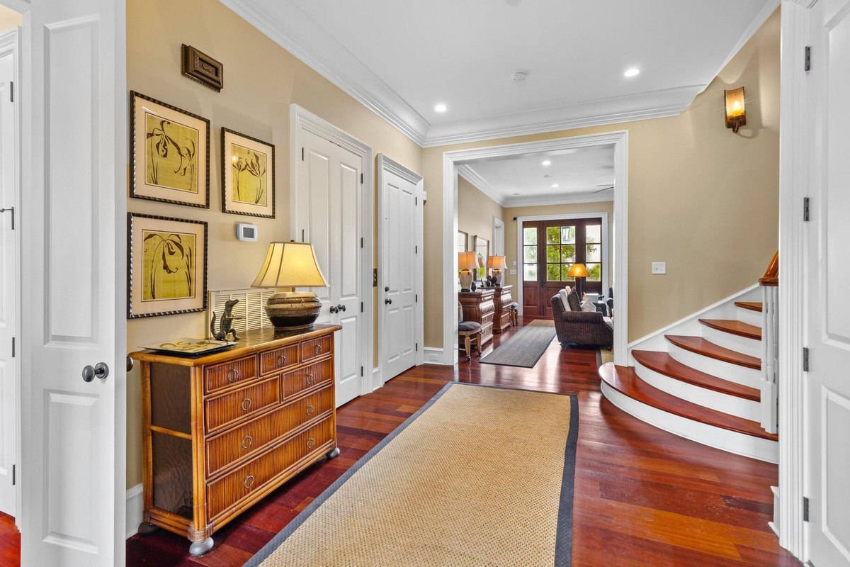 Entryway features hardwood floors, a curved staircase, and a rattan dresser with artwork.