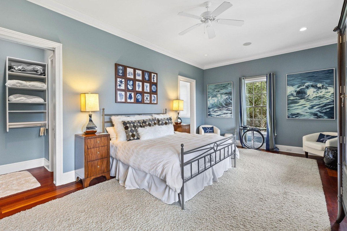 Master bedroom features a bed with metal frame, ocean-themed artwork, and a fluffy white rug.