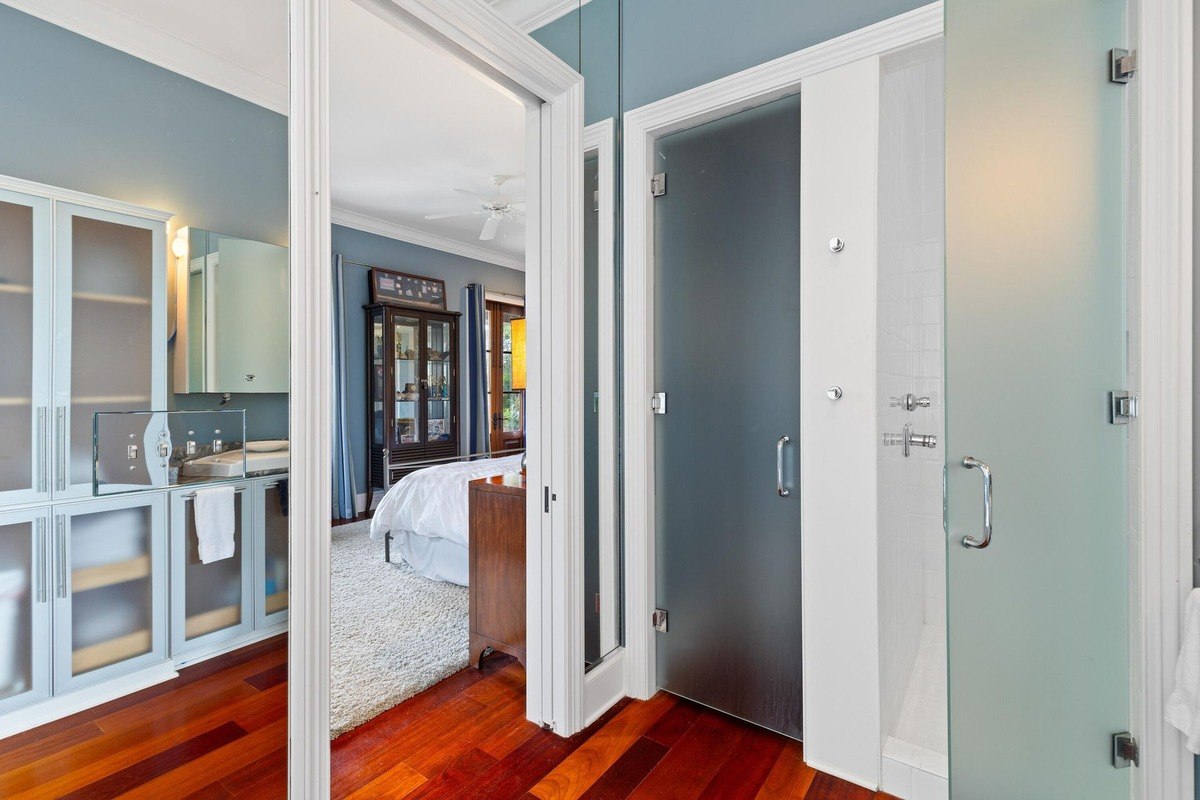 Bathroom hallway shows a bedroom, frosted glass shower doors, and hardwood floors.