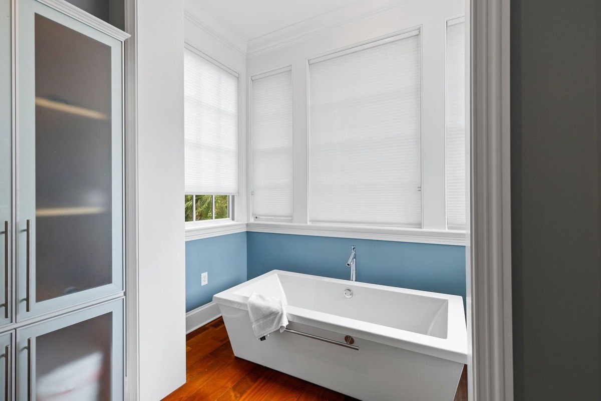 Modern bathroom features a freestanding tub, light blue walls, and hardwood floors.