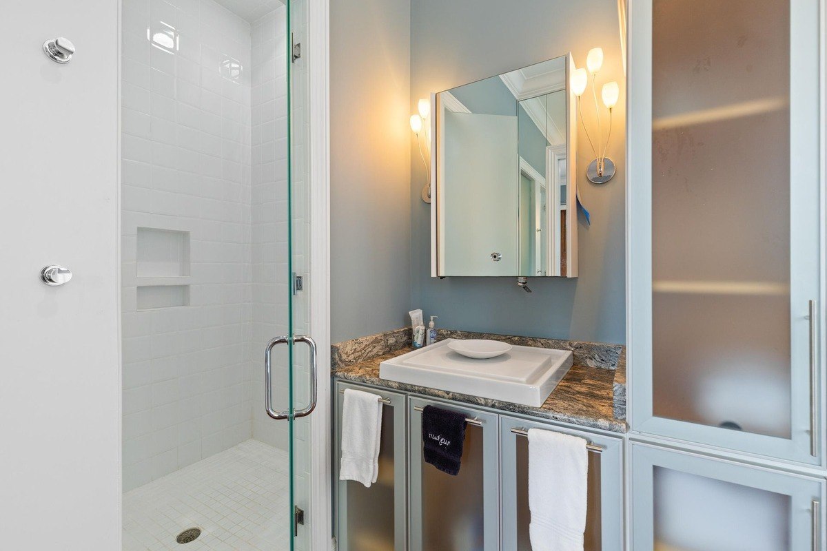 Bathroom features a white sink, granite countertop, glass shower enclosure, and light blue walls.