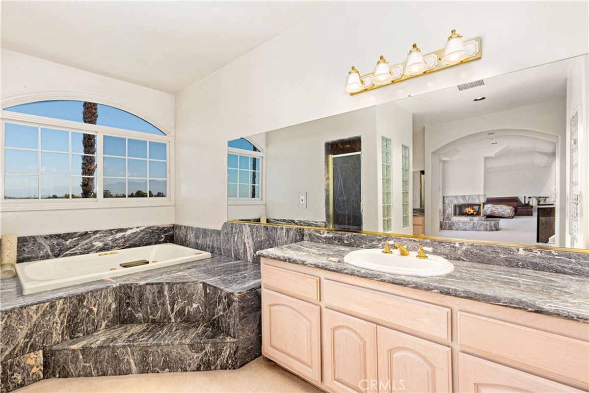 Luxurious bathtub area with marble finish sits beside a large window.