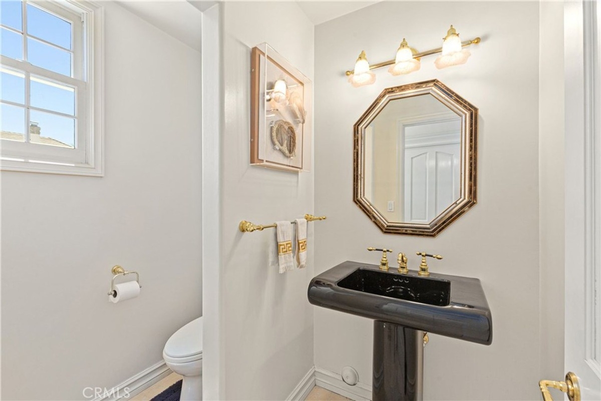 Compact bathroom includes a black pedestal sink and gold fixtures.