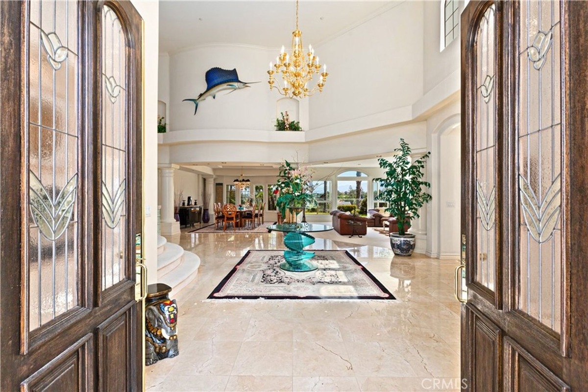 Grand entrance with double wooden doors opening to a marble-floored foyer and chandelier.