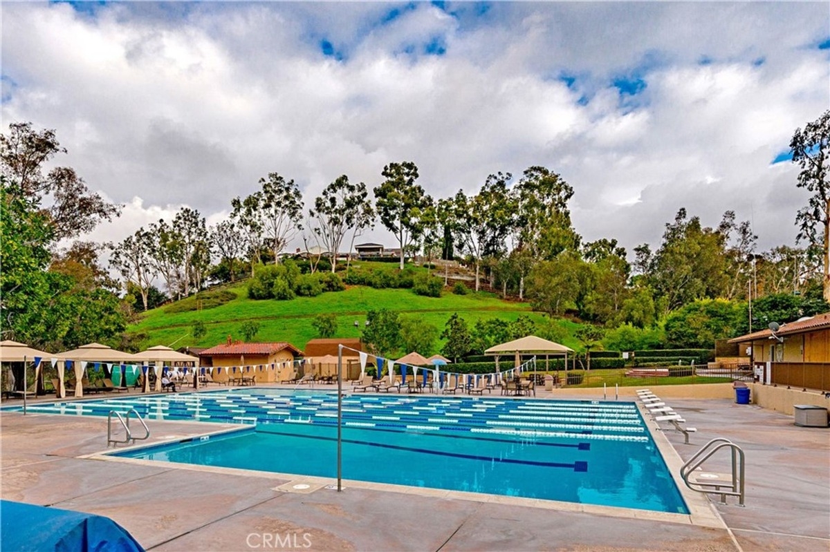 Swimming pool area with lap lanes, cabanas, and a scenic green hill in the background.