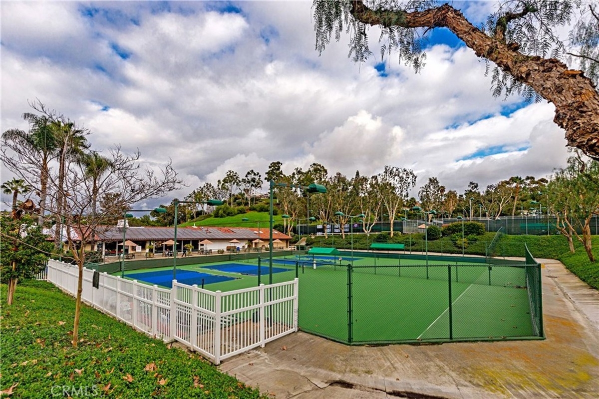 Tennis courts enclosed by fencing, featuring multiple play areas and greenery surrounding the facility.