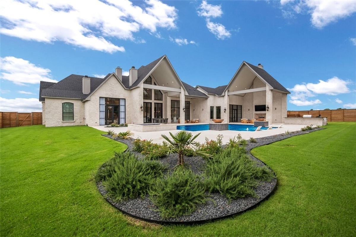 Backyard view of a large, modern house with a swimming pool and landscaped lawn.