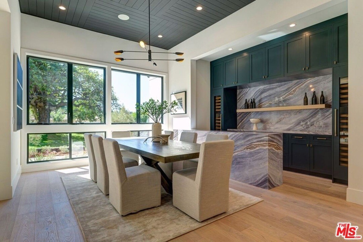 Elegant dining area combines neutral seating with a wooden table, marble backsplash, and integrated cabinetry for wine storage.