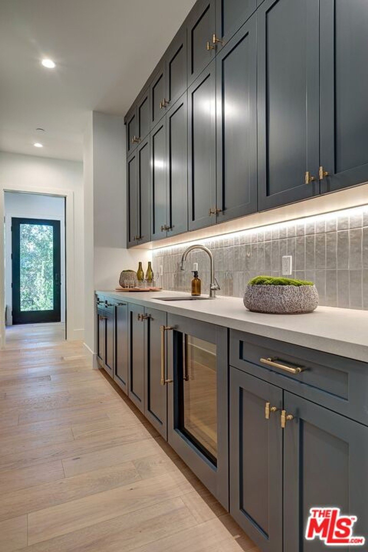 Hallway wet bar area showcases tall cabinetry, a sink, and built-in beverage cooler illuminated by accent lighting.