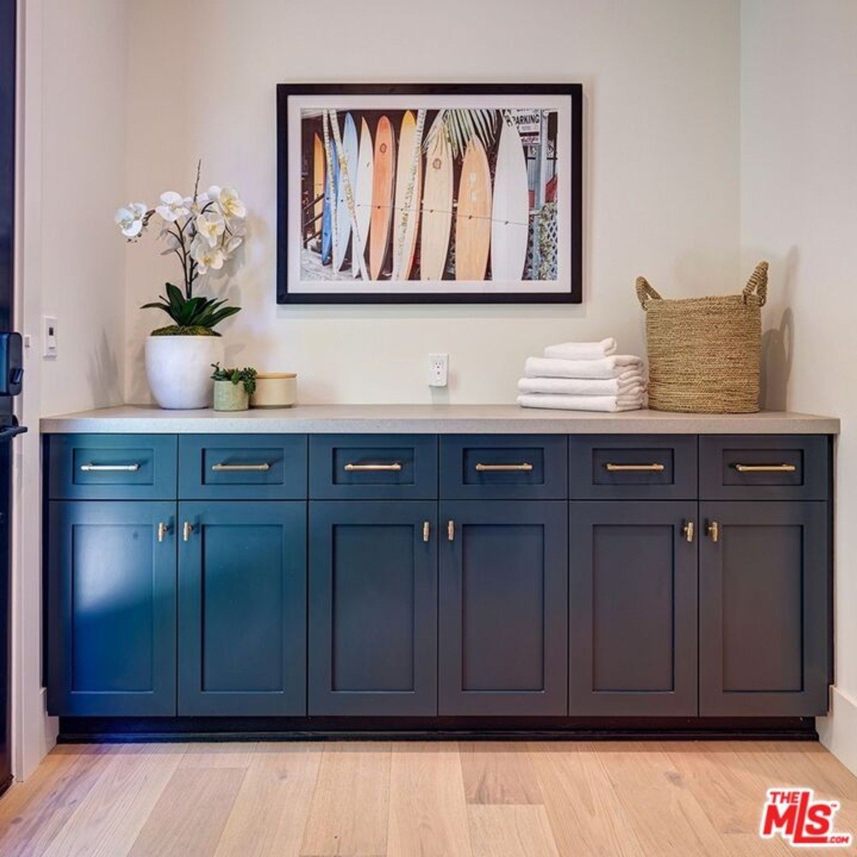 Countertop space adorned with surfboard artwork above cabinetry and styled with decor elements like a woven basket and floral arrangement.