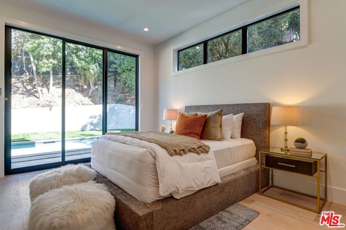 Primary bedroom displays a cushioned platform bed, glass sliding doors to the backyard, and plush accent furniture placed at the foot.