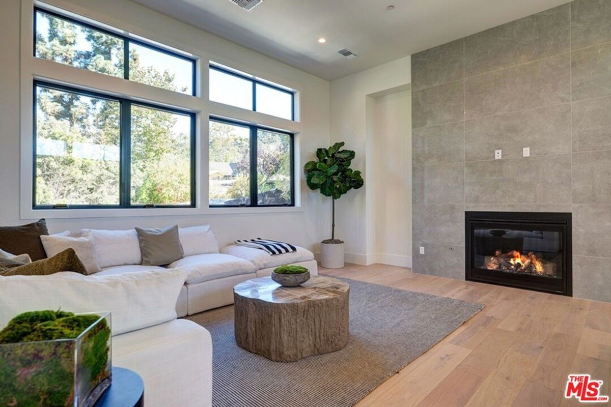 Living area featuring a large sectional sofa, a rustic wooden coffee table, and a fireplace set within a sleek stone wall.