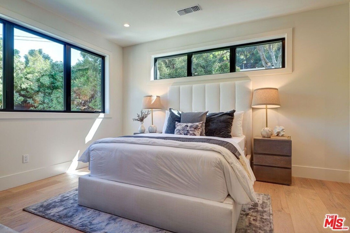 Bright bedroom with a tufted cream headboard, neutral bedding, and large windows that fill the space with natural light.