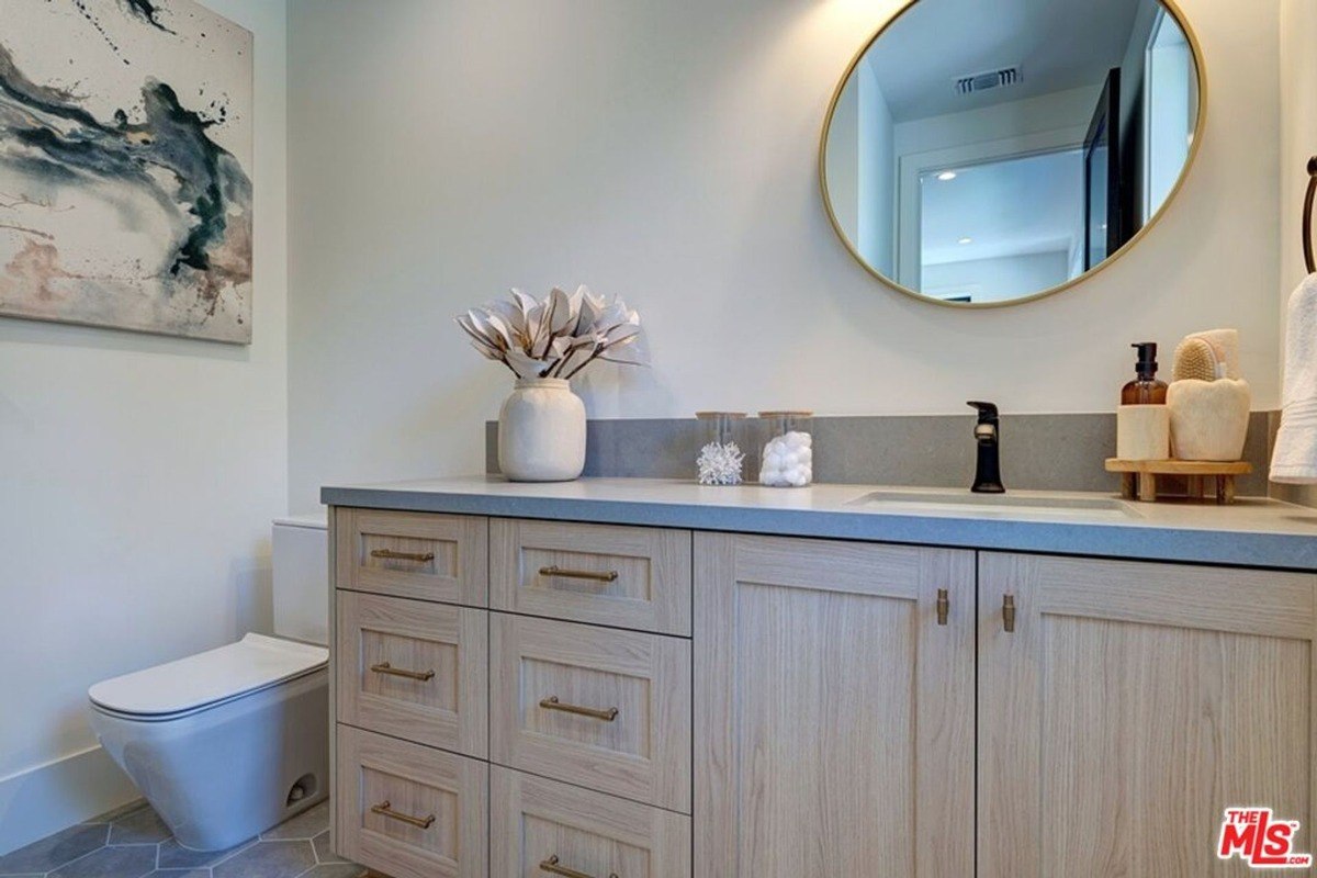 Bathroom vanity topped with a gray countertop, decorated with a round mirror and ceramic accents for a clean, contemporary look.