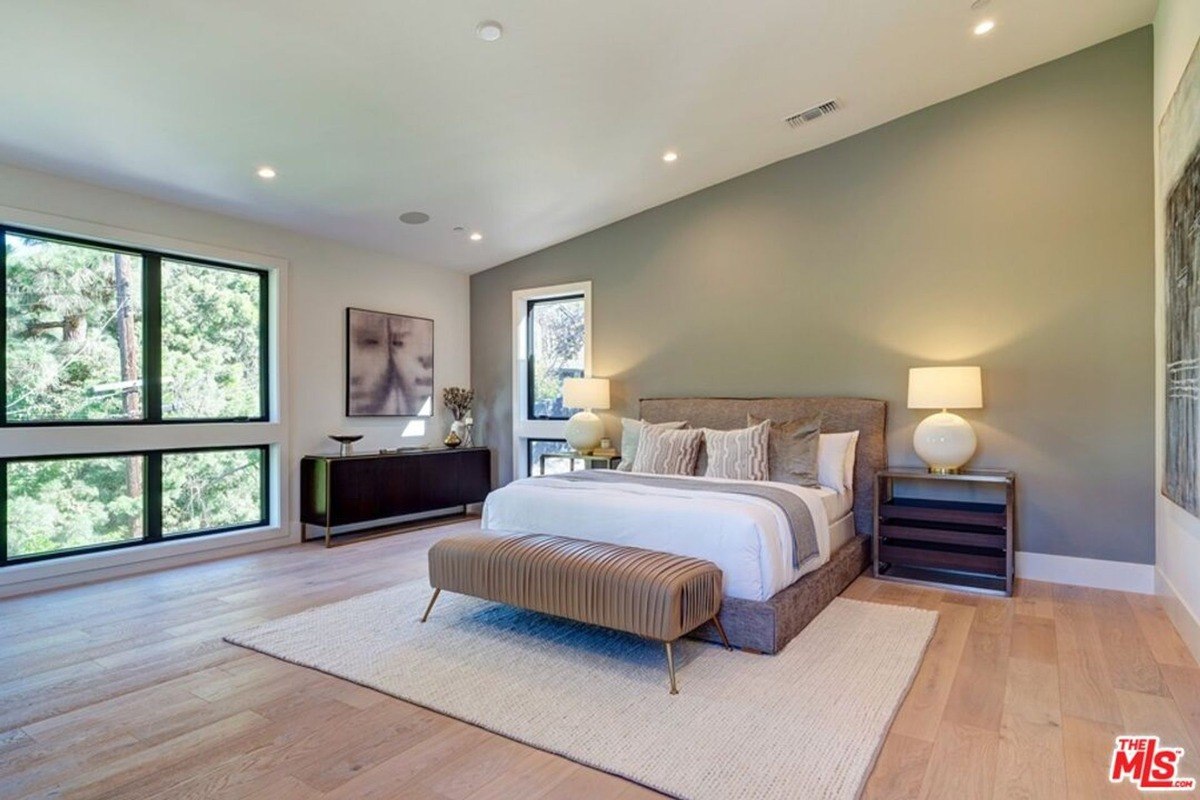 Modern bedroom setup features a gray accent wall, large windows, and a sleek platform bed with neutral-toned bedding.