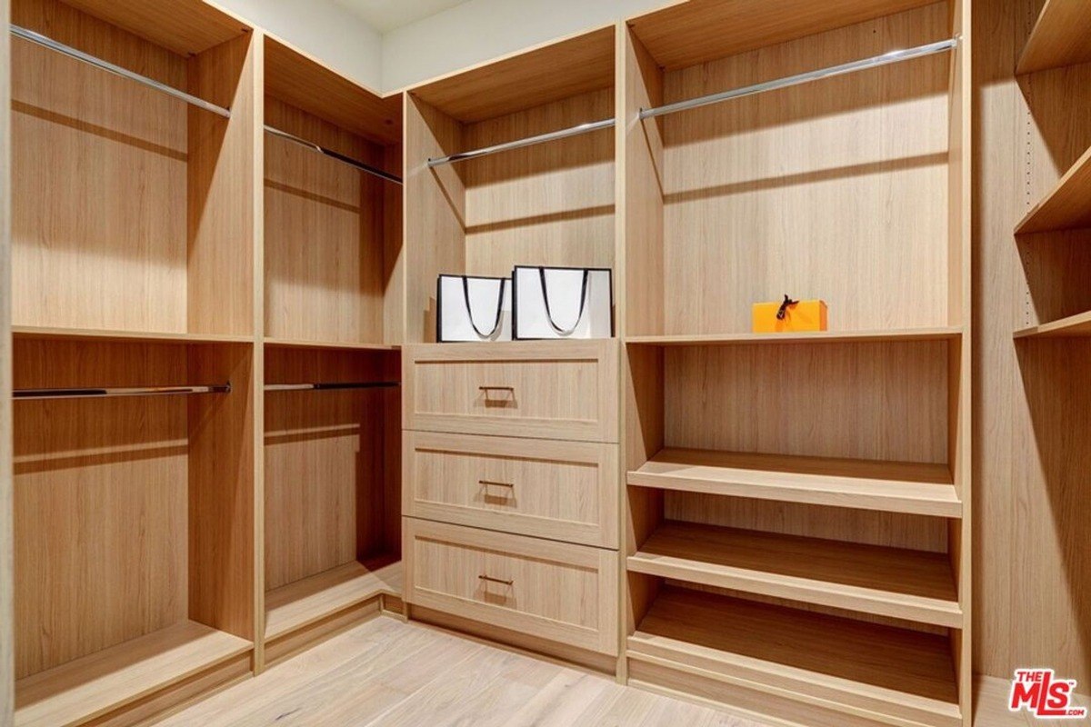 Spacious walk-in closet offers custom wooden shelves, drawers, and multiple hanging spaces for organization.