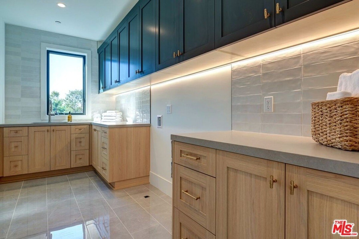 Modern utility area features natural wood lower cabinets, dark blue upper cabinetry, under-cabinet lighting, and a window bringing in natural light.