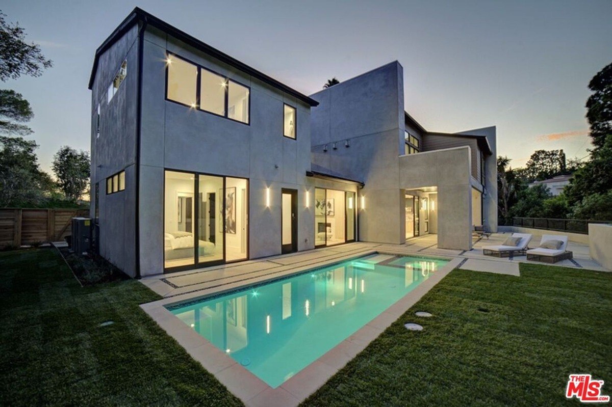 Home exterior features expansive windows and a sleek pool surrounded by a manicured lawn.